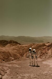 Two astronauts in spacesuits exploring a desolate, Mars-like desert landscape.