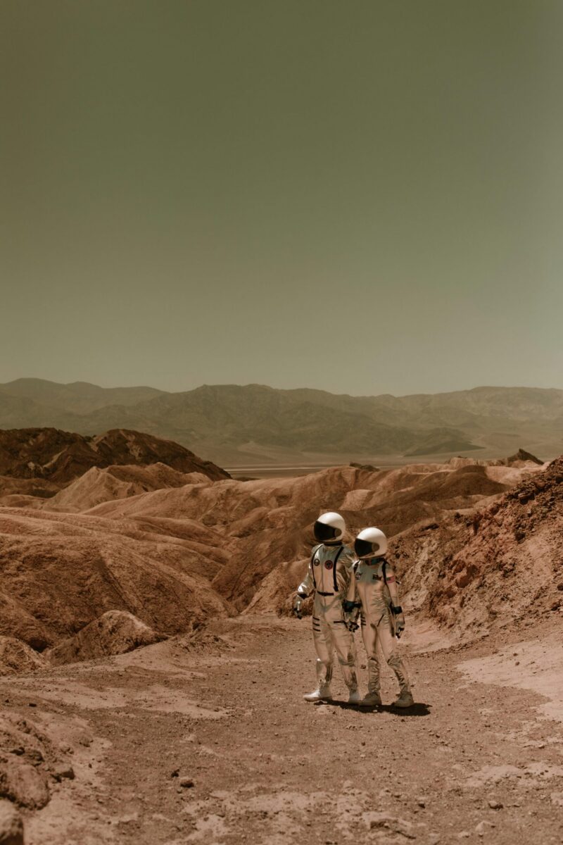 Two astronauts in spacesuits exploring a desolate, Mars-like desert landscape.
